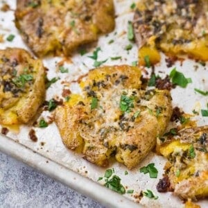 Golden brown potato smashed on sheet pan, sprinkled with parmesan cheese and fresh parsley.