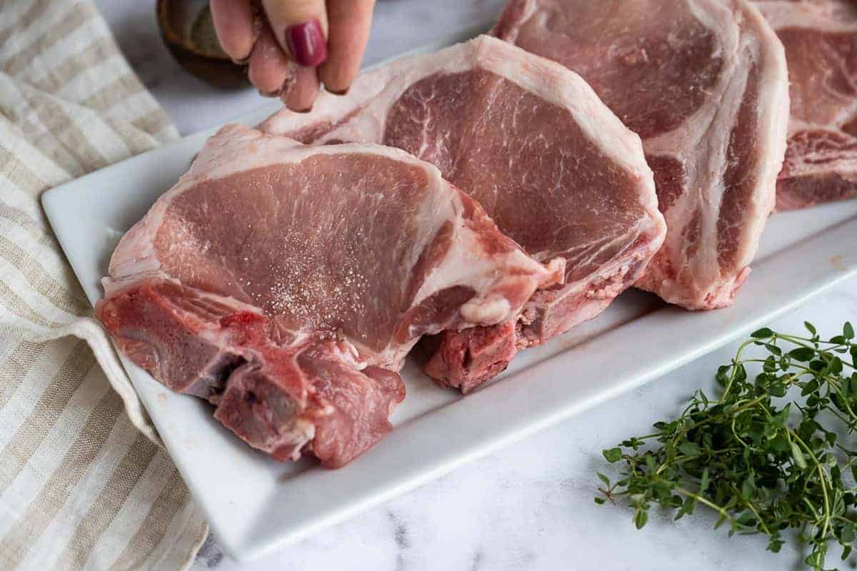 Pork chops being seasoned with salt and pepper.