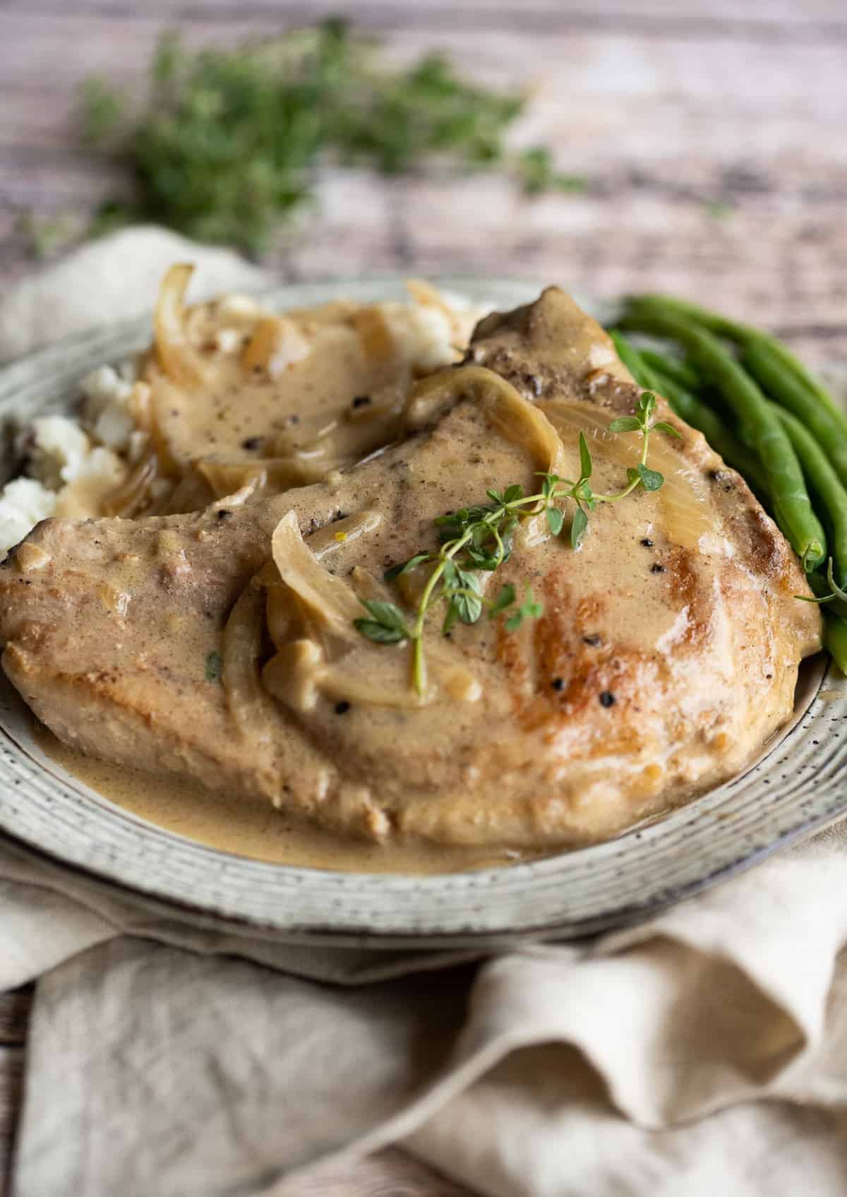 Pork on a plate with mushroom gravy and a side of green beans.