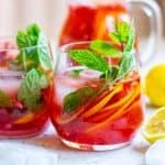 Brightly colored red drink in a stemless glass, full of citrus slices and mint leaves.