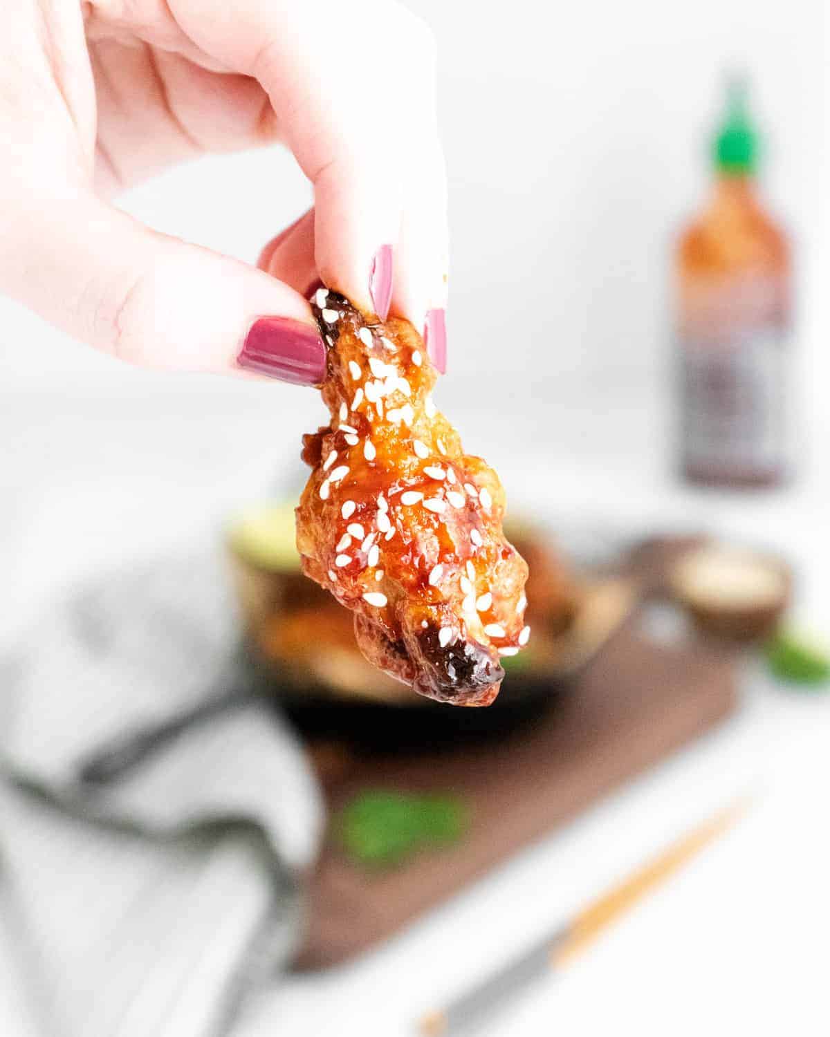 Hand holding a wing sprinkled with sesame seeds.
