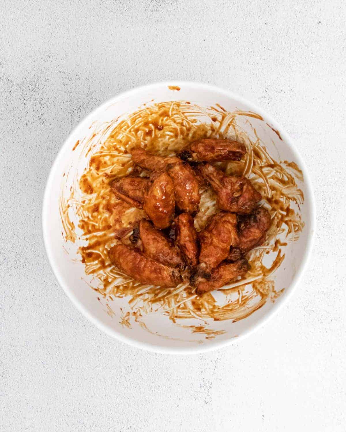 Wings being tossed with sauce in a white bowl.