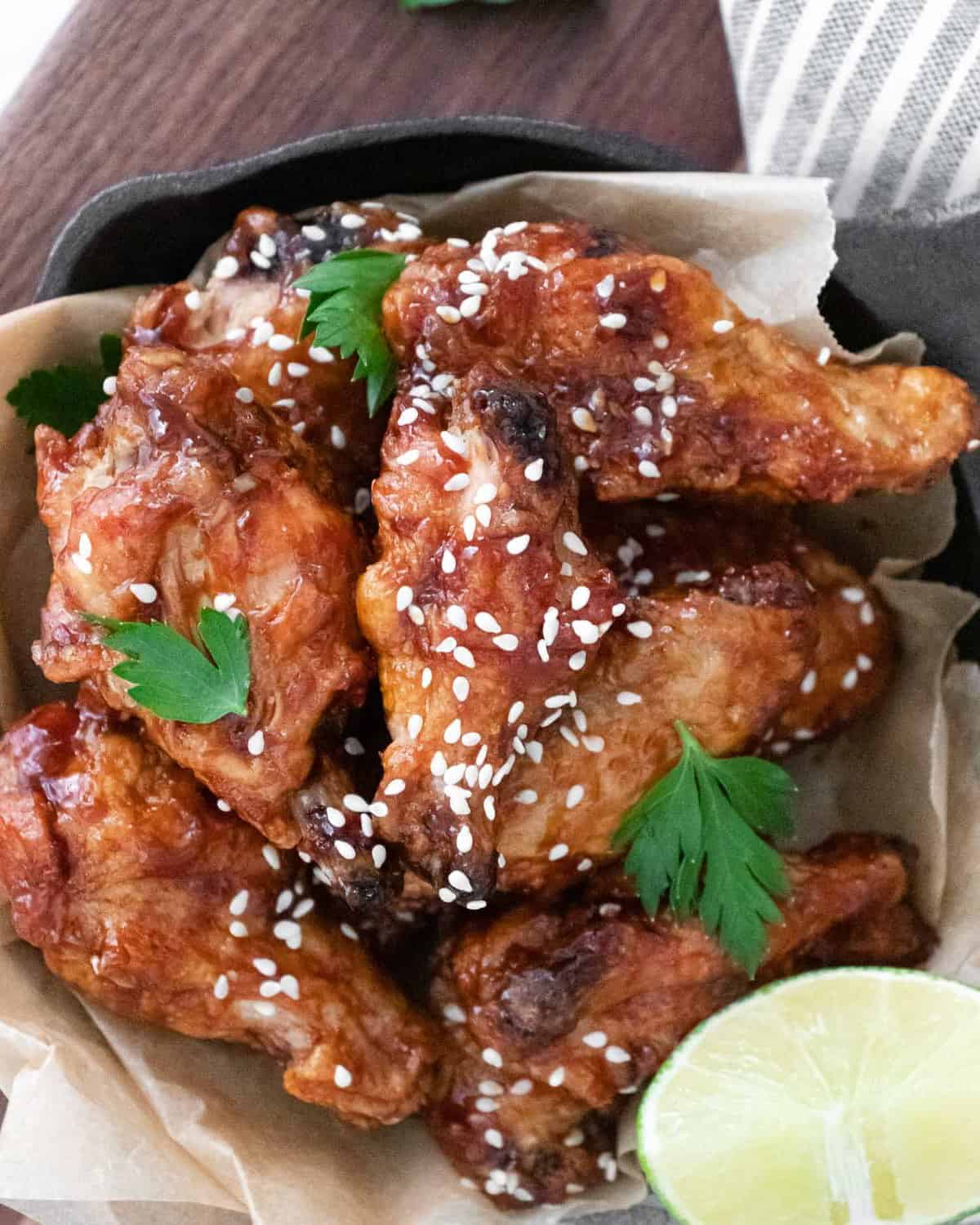 Overhead view of asian chicken wings in a basket with lime pieces and sesame seeds.