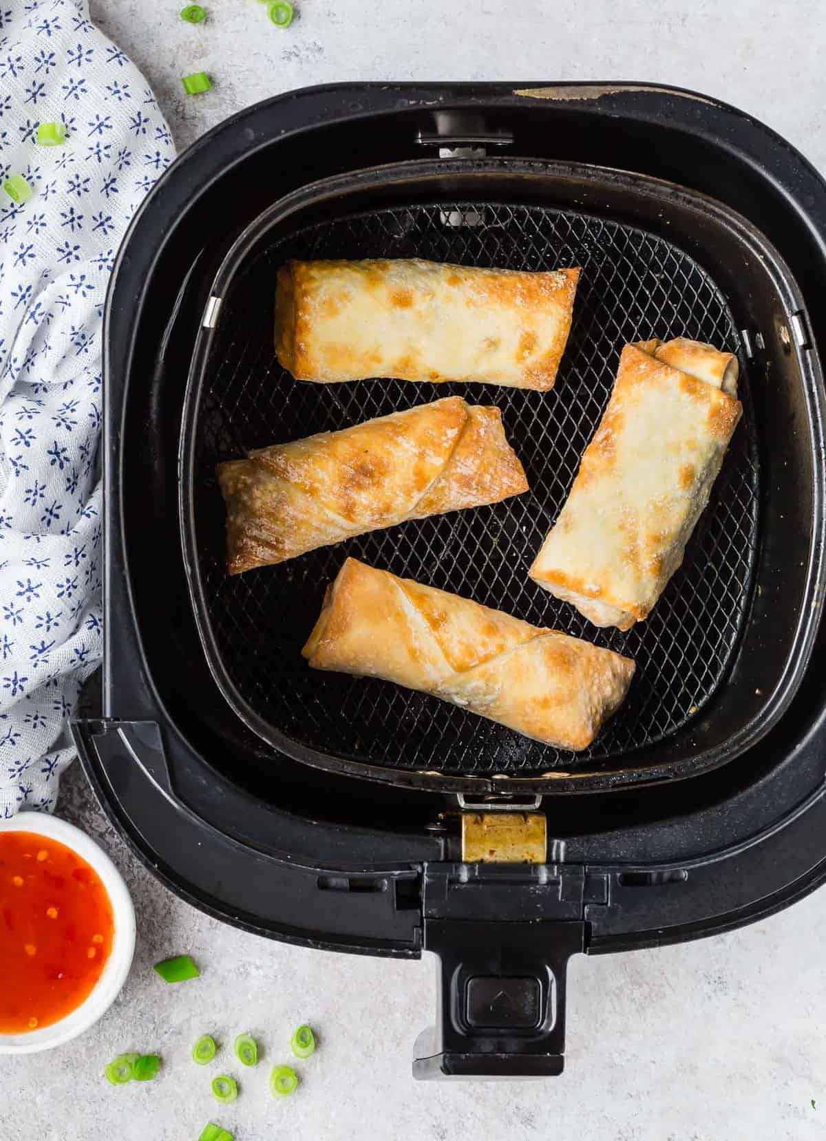 Overhead view of a air fryer basket with egg rolls in it.
