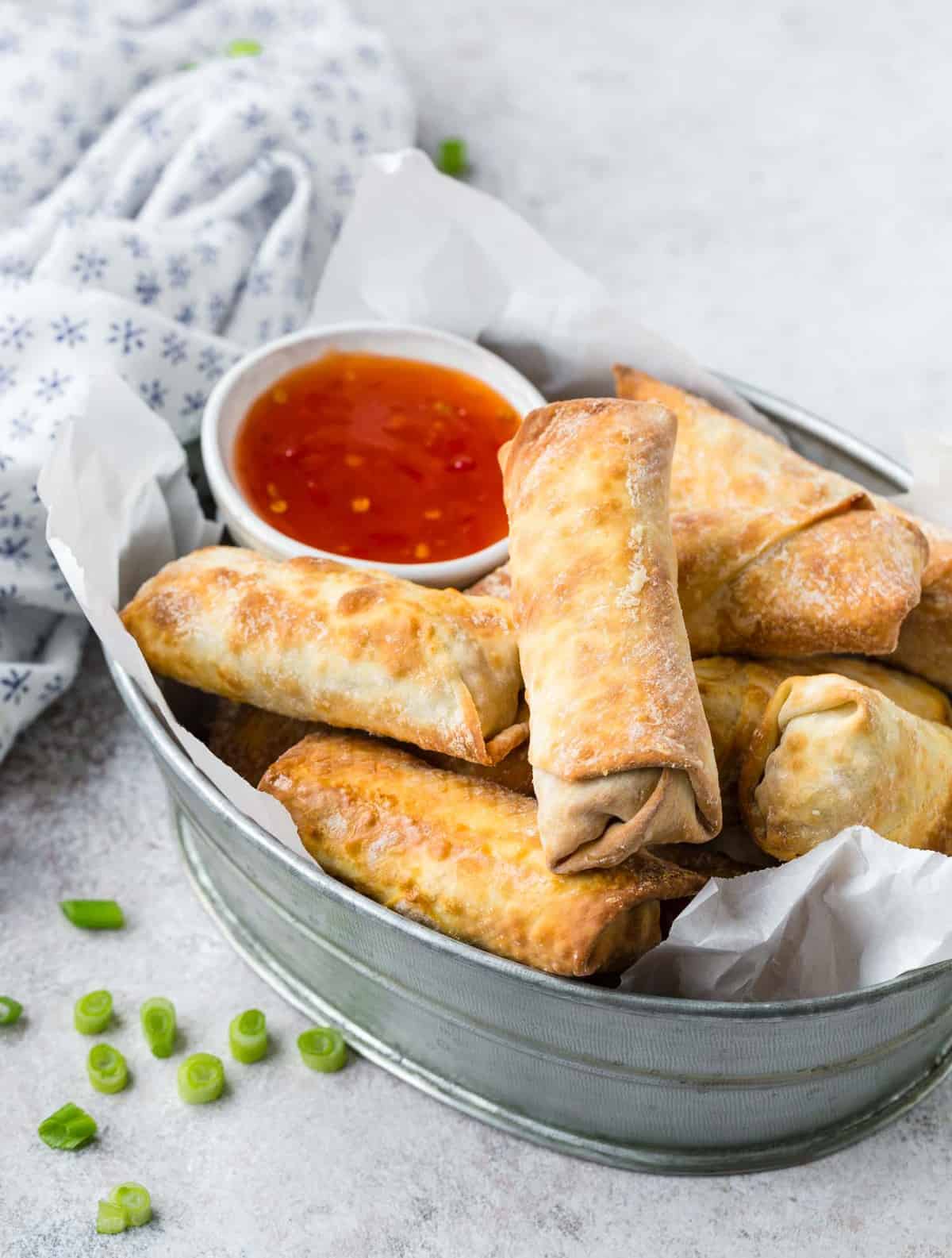 Egg rolls in a metal basket with dipping sauce.