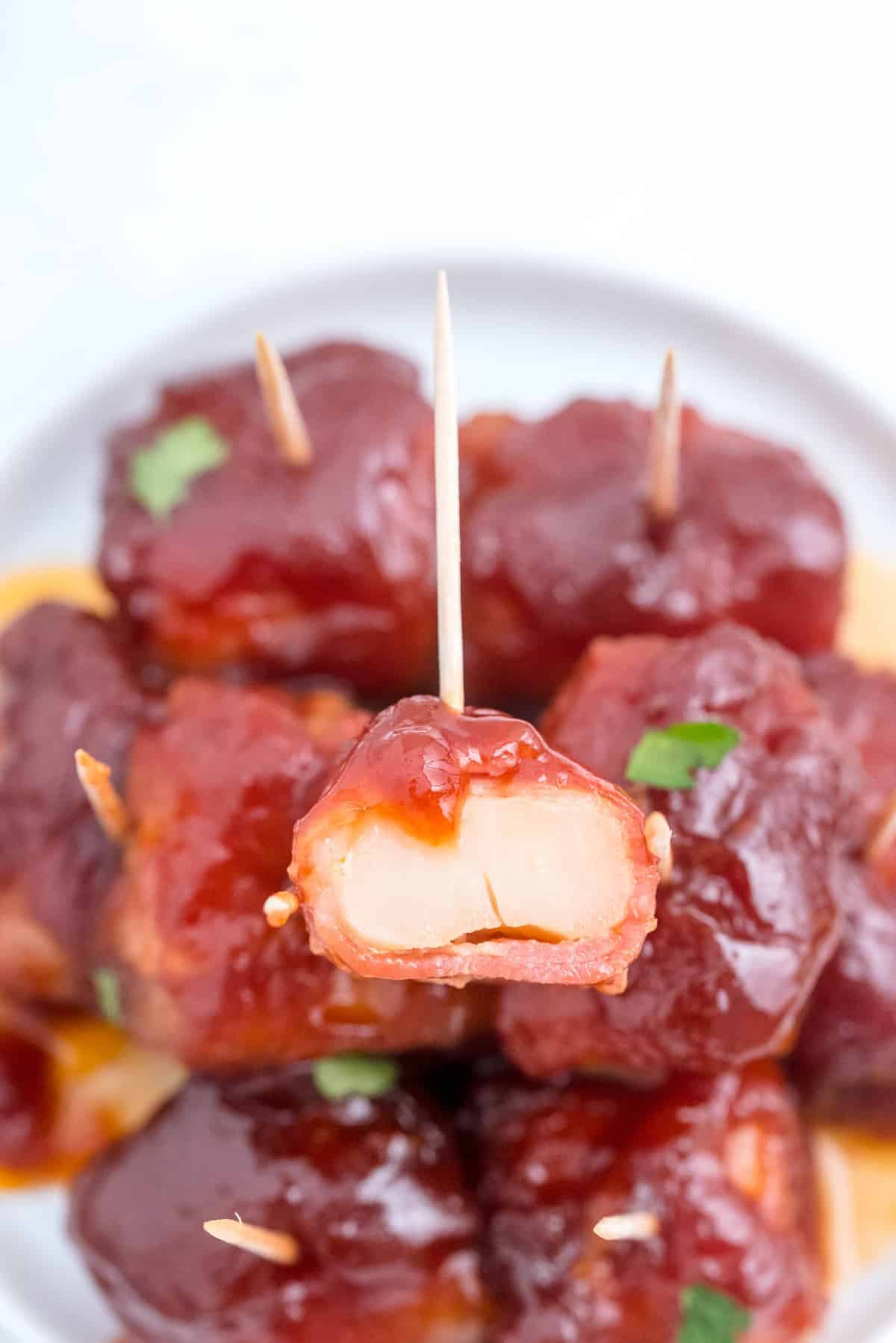 One bacon wrapped water chestnut cut in half, on top of a pile of whole ones with toothpicks.