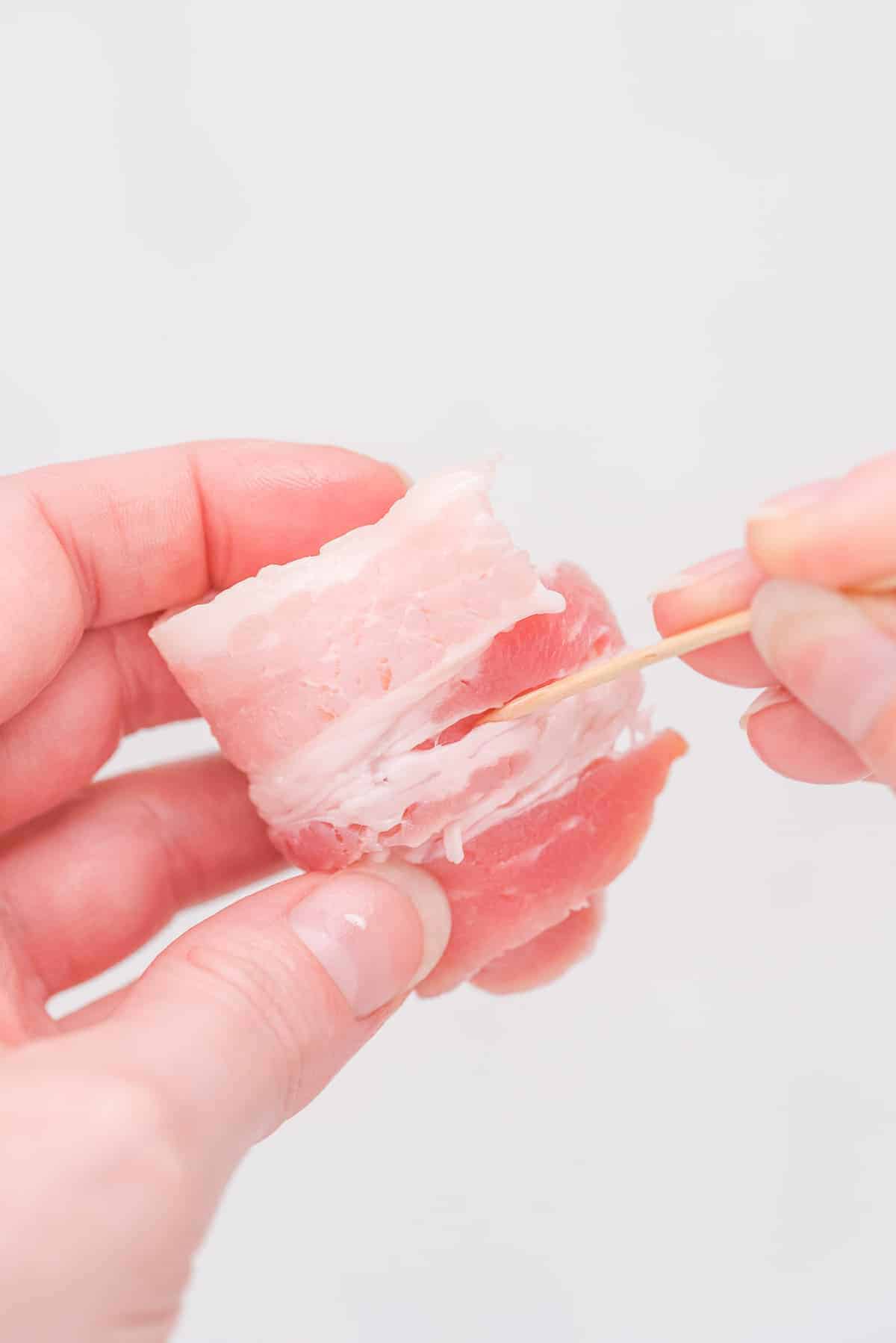 Toothpick being stuck into an uncooked bacon wrapped water chestnut.