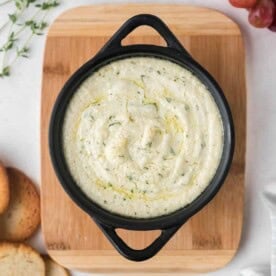 Overhead view of a small black pan with goat cheese dip, sprinkled with fresh thyme.