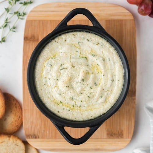 Overhead view of a small black pan with goat cheese dip, sprinkled with fresh thyme.
