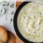 Dip in a black pan with a small pieces of crisp bread. Text overlay reads "baked goat cheese dip with lemon and thyme, rachelcooks.com"