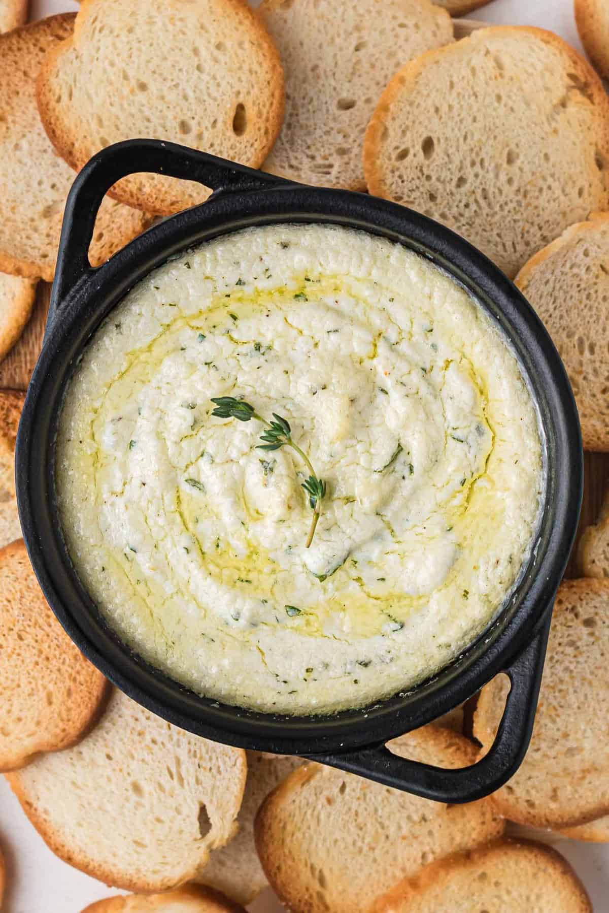 Close up of a baked goat cheese dip in a black cast iron pan.
