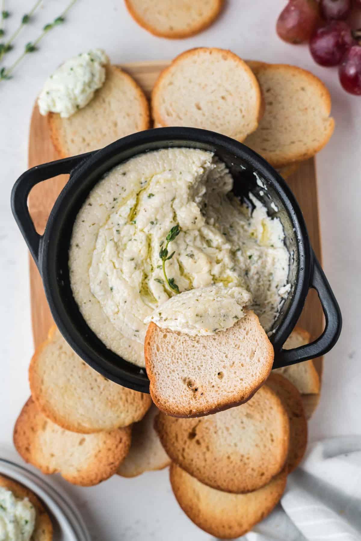 Bread being dipped into goat cheese dip in a black pan.