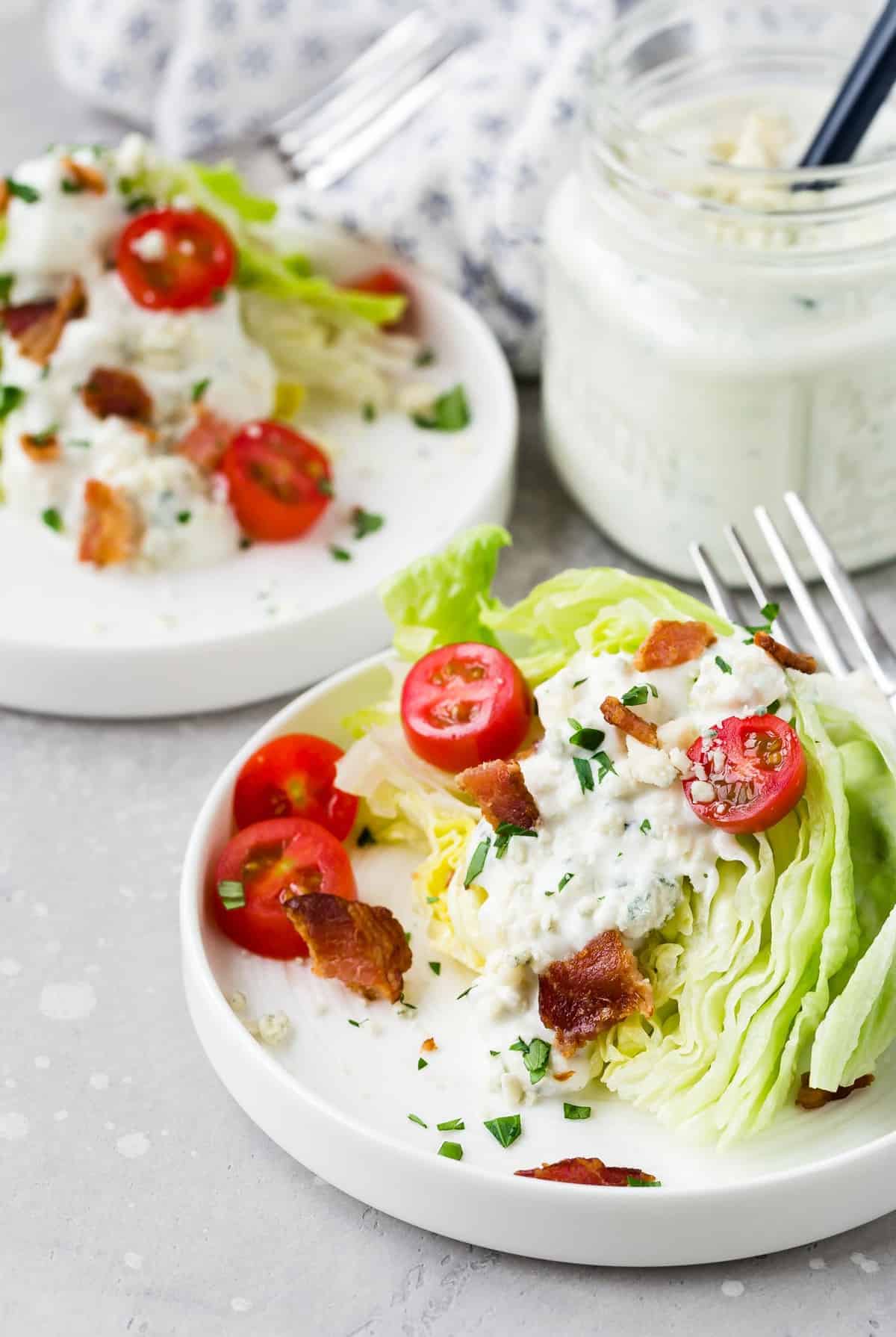 Two plates of salad with a jar of dressing in the background.