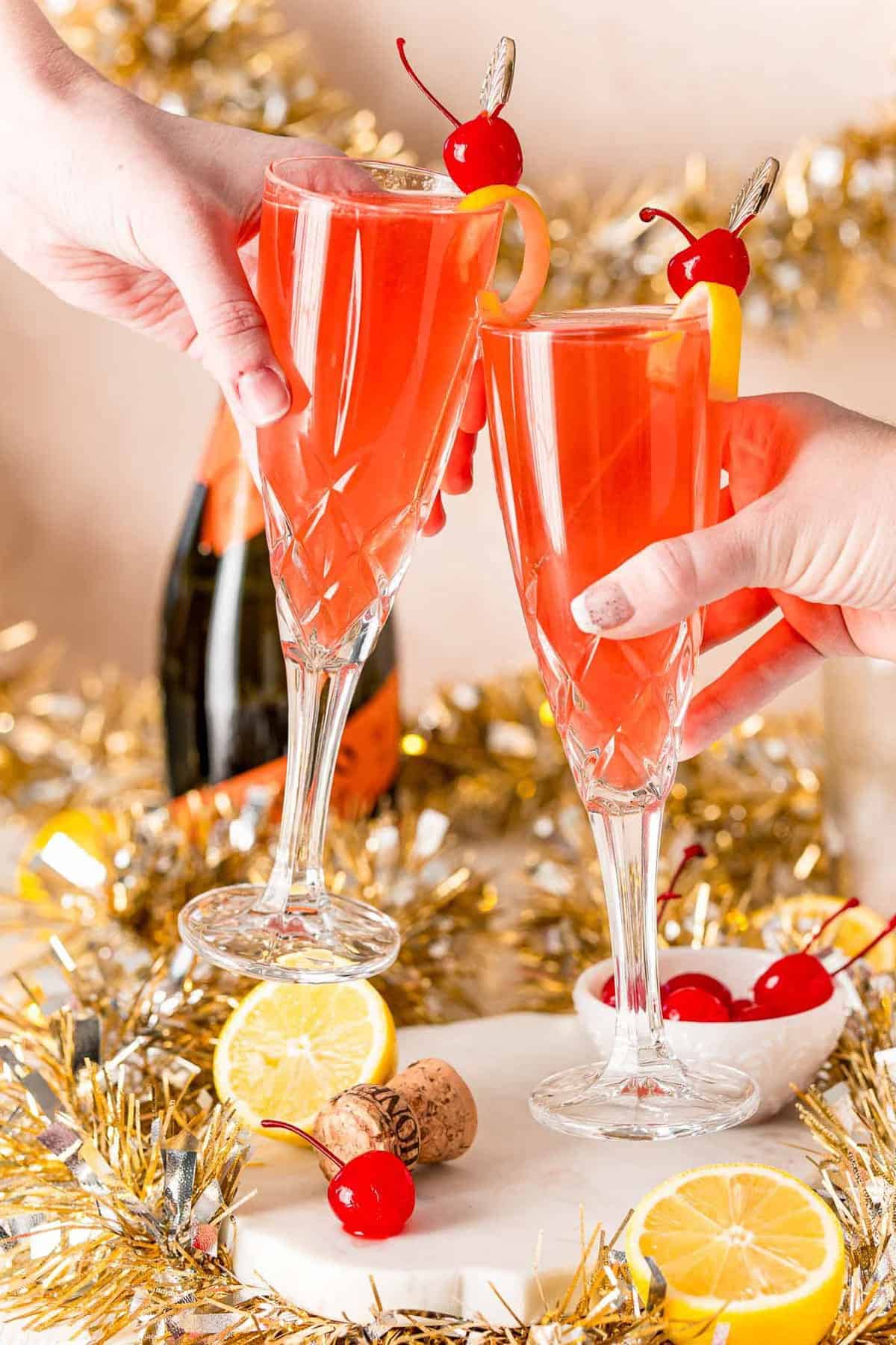 A champagne toast with light red liquid in champagne glasses.