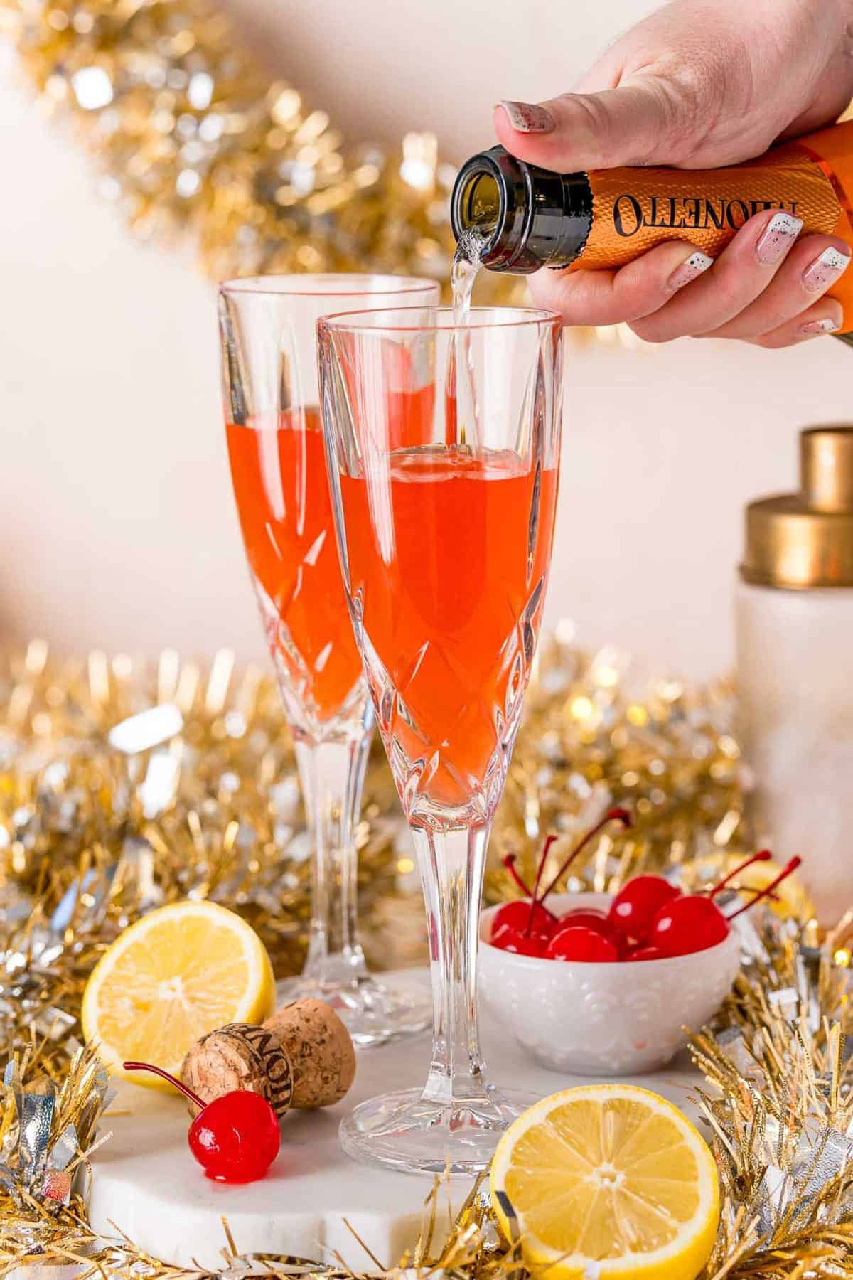 Champagne being poured into a champagne glass already partially full of light red liquid.