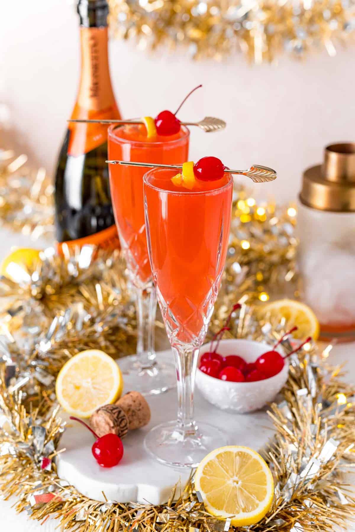 Festive scene with two champagne glasses, lemons, cherries, and gold garland.