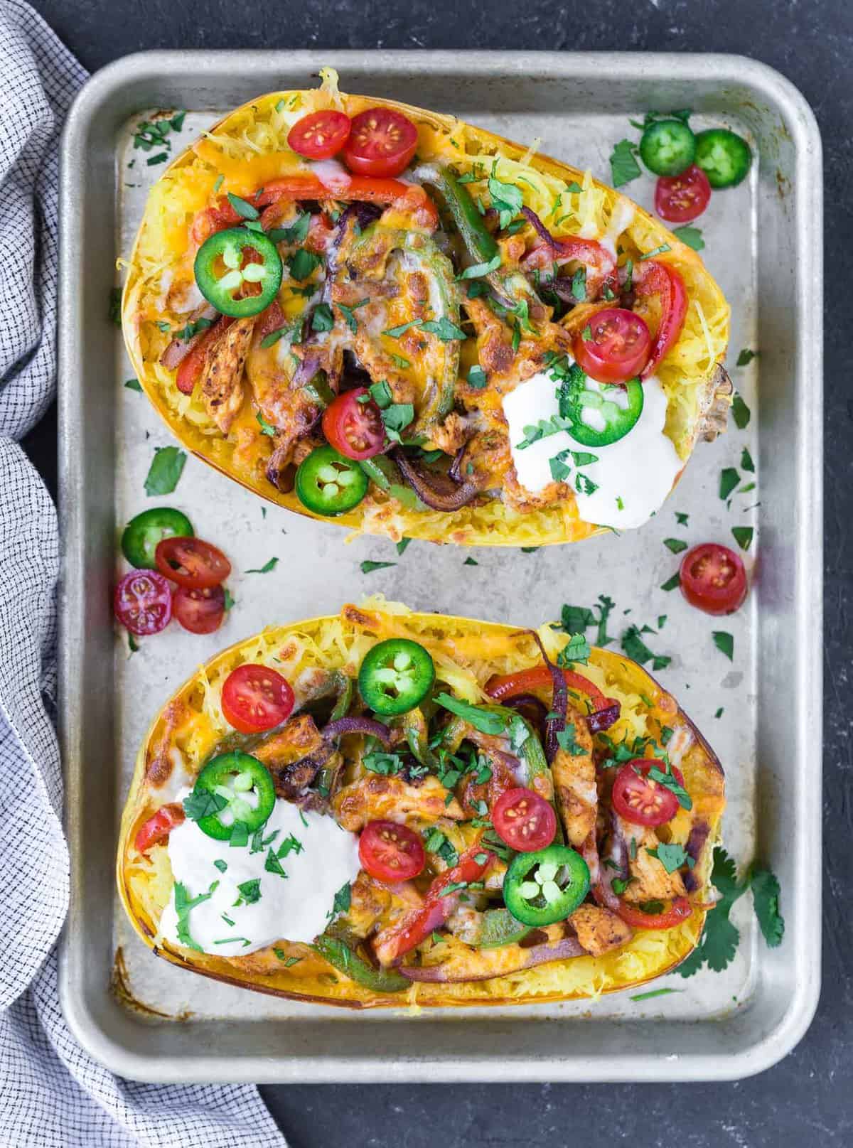 Two halves of a spaghetti squash, topping with fajita toppings.