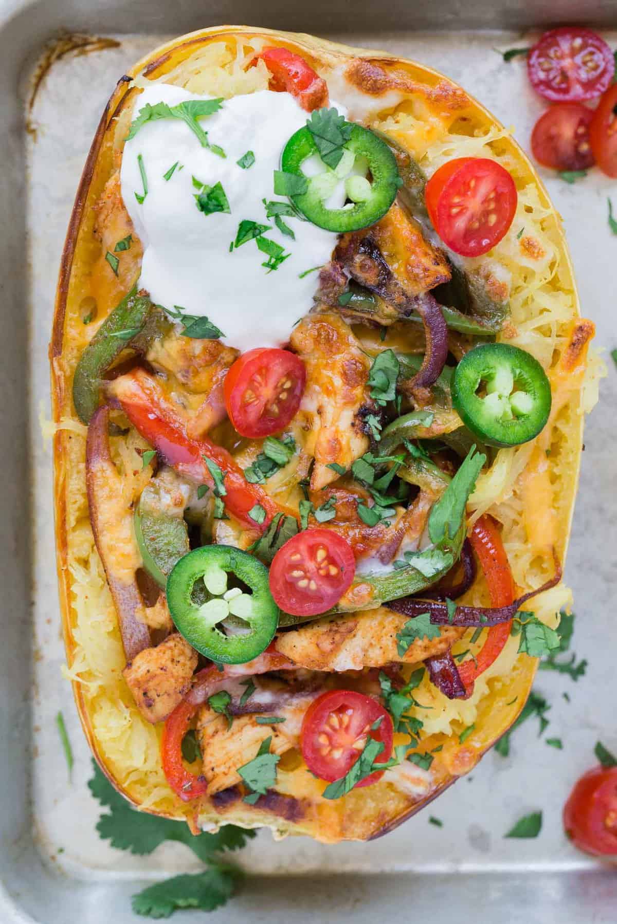 Overhead view of a spaghetti squash half, stuffed with chicken, bell peppers, and topped with fajita toppings.