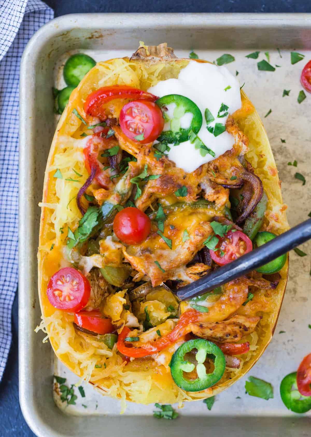 A fork stuck in a spaghetti squash that has been filled with chicken fajita toppings.