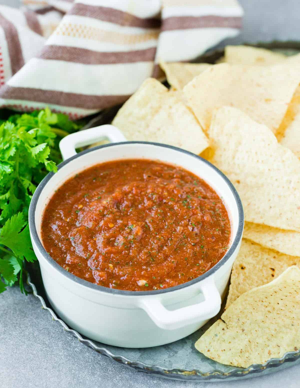 Blender salsa in a bowl, surrounded by chips and cilantro.