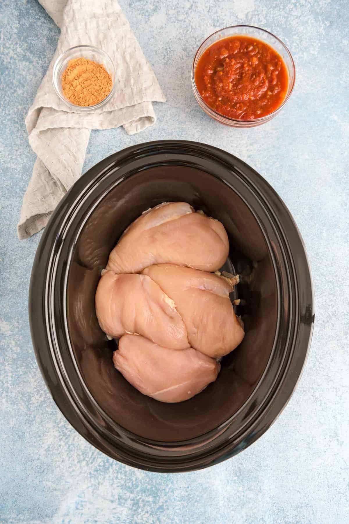 Raw chicken breasts in a black slow cooker.