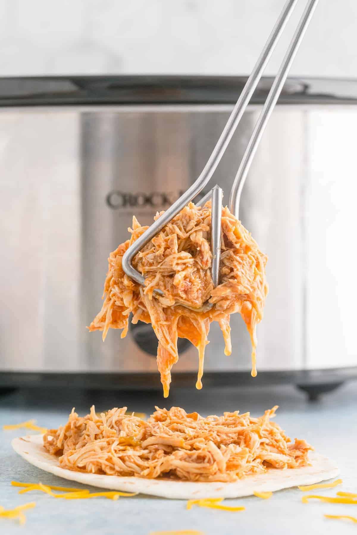 Shredded chicken in tongs in front of a crockpot.