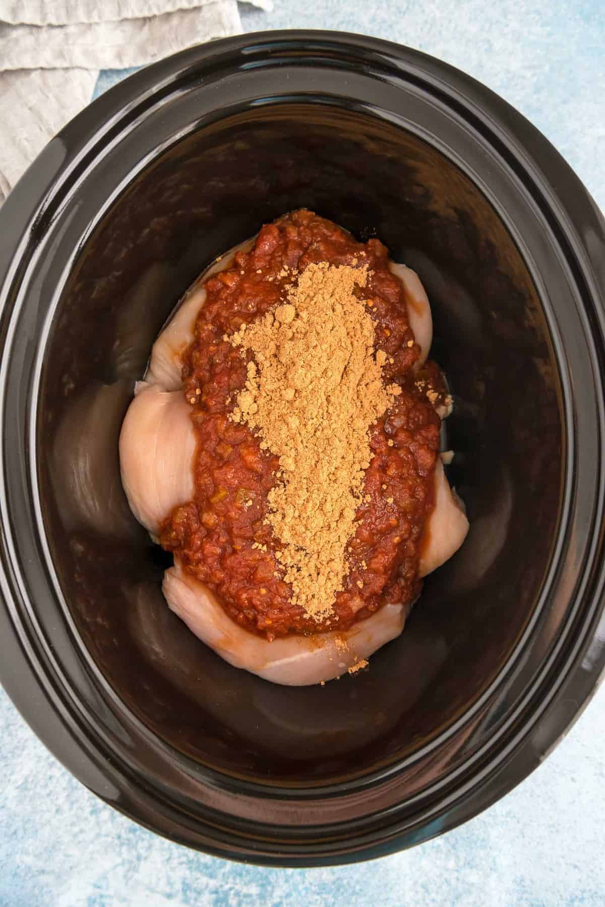 Chicken, salsa, and taco seasoning in a slow cooker.