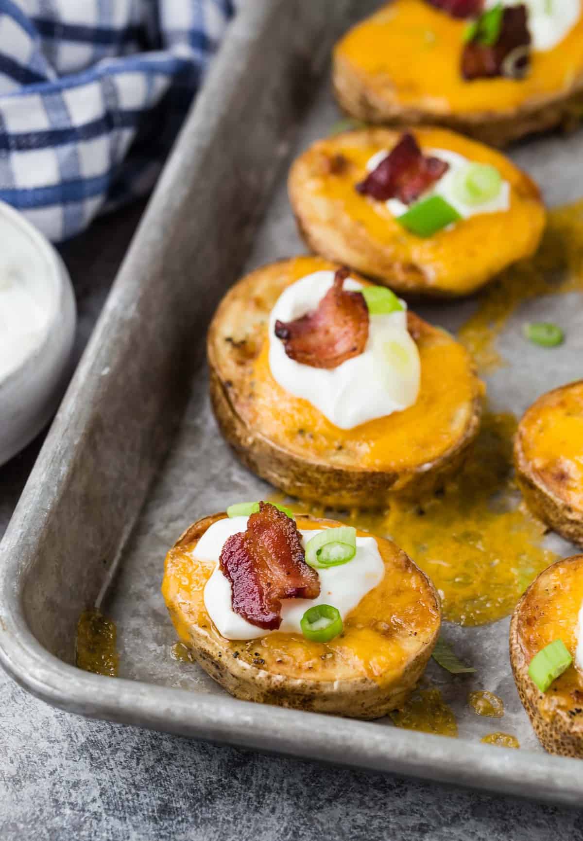 Potato rounds on a pan, topped with cheese, sour cream, bacon, green onion.