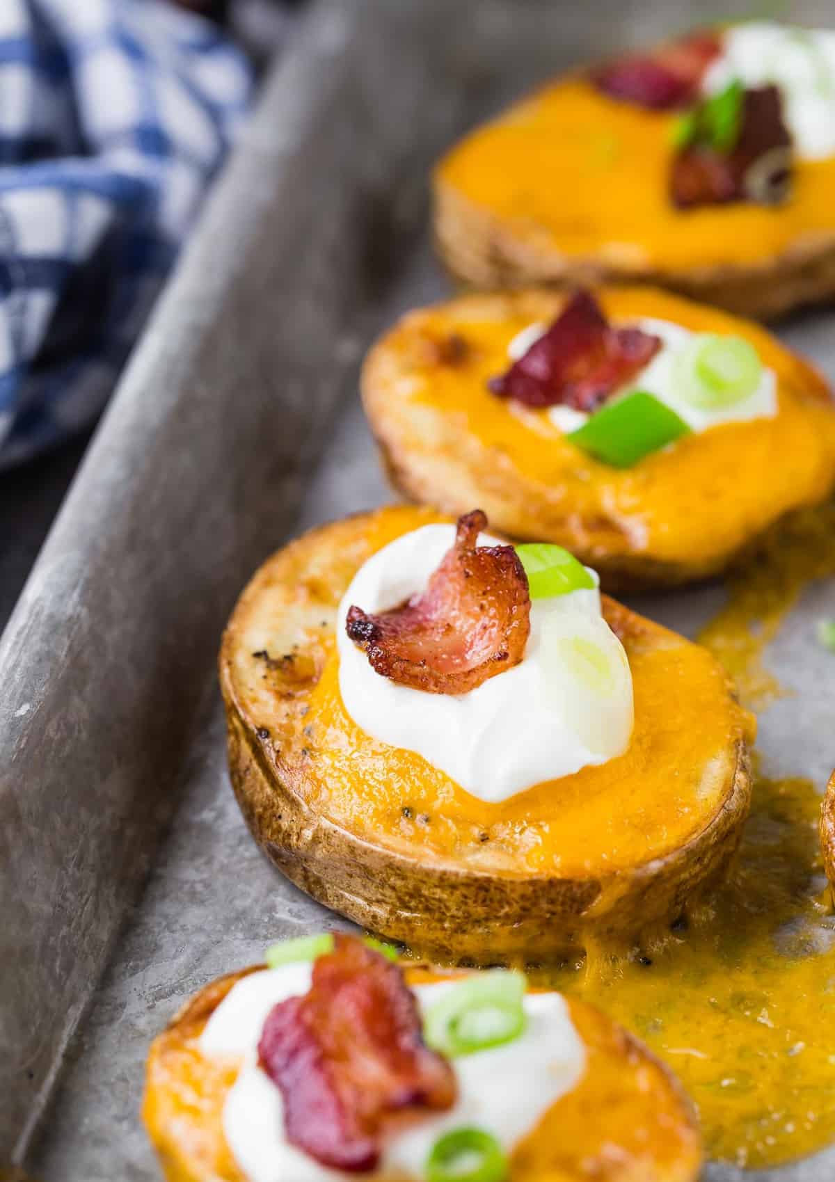 Sliced potatoes with cheese and toppings on a baking sheet. 