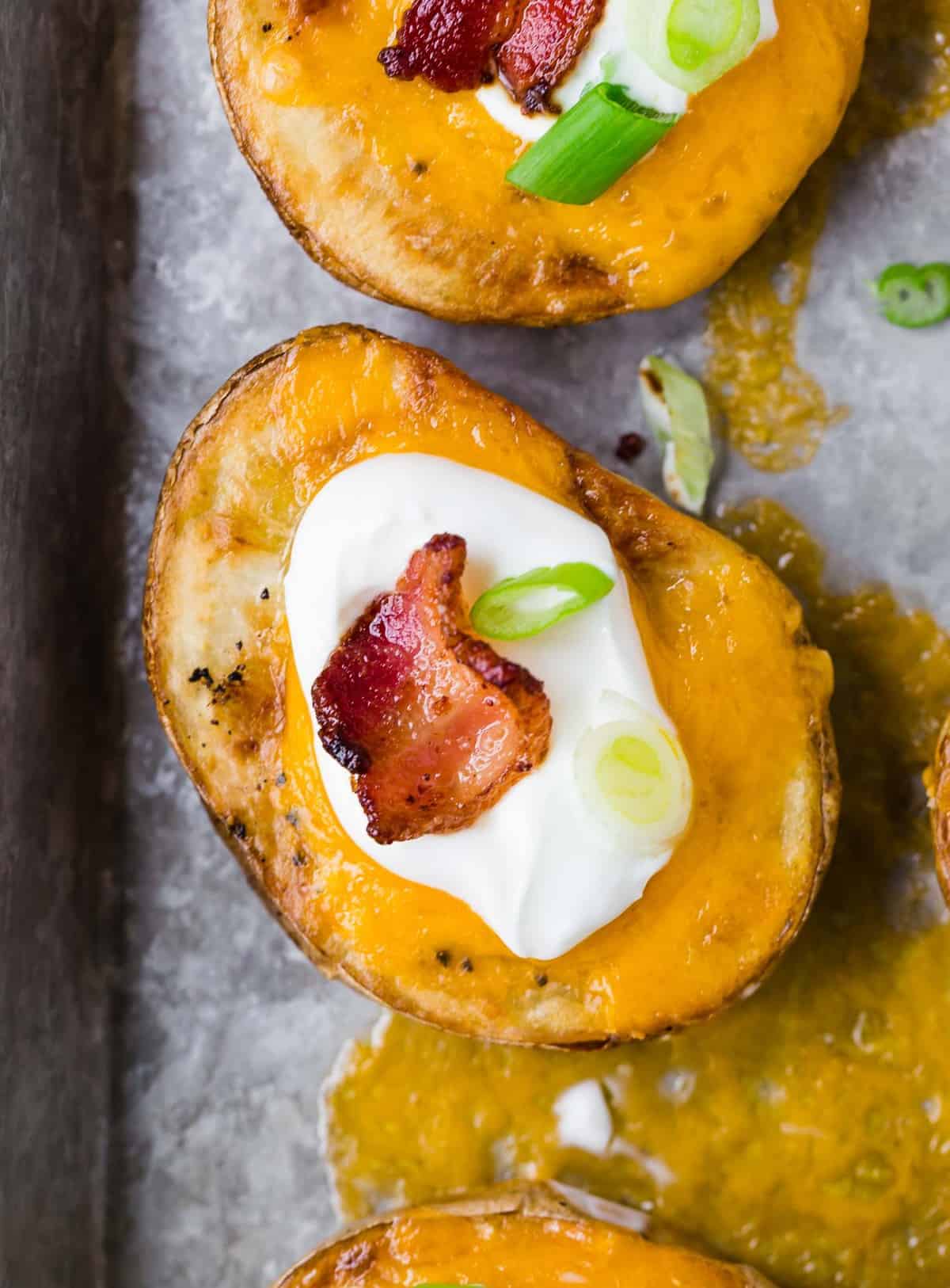 Overhead view of a slice of potato on a tray, covered with cheese, and topped with sour cream, bacon, and green onion.