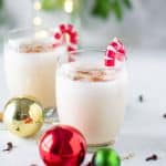 Two small glasses of egg nog garnished with candy cane ornaments.