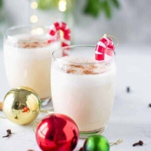 Two small glasses of egg nog garnished with candy cane ornaments.