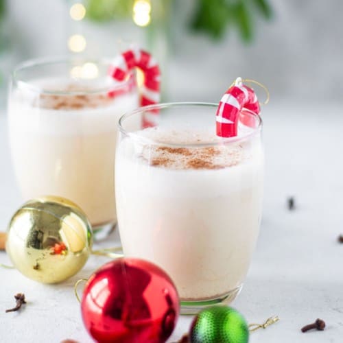 Two small glasses of egg nog garnished with candy cane ornaments.