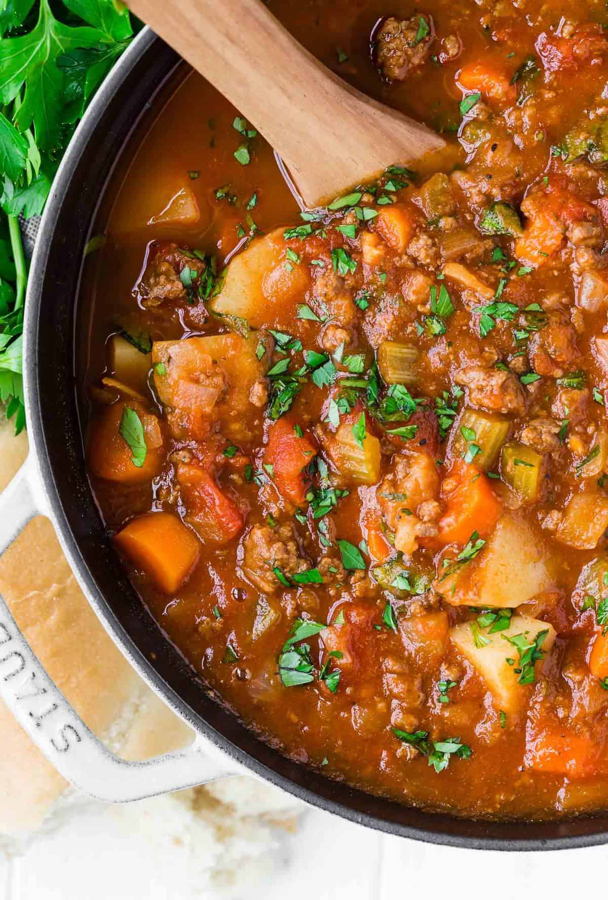 Large pot of hamburger soup with potatoes and carrots, with a wooden spoon.