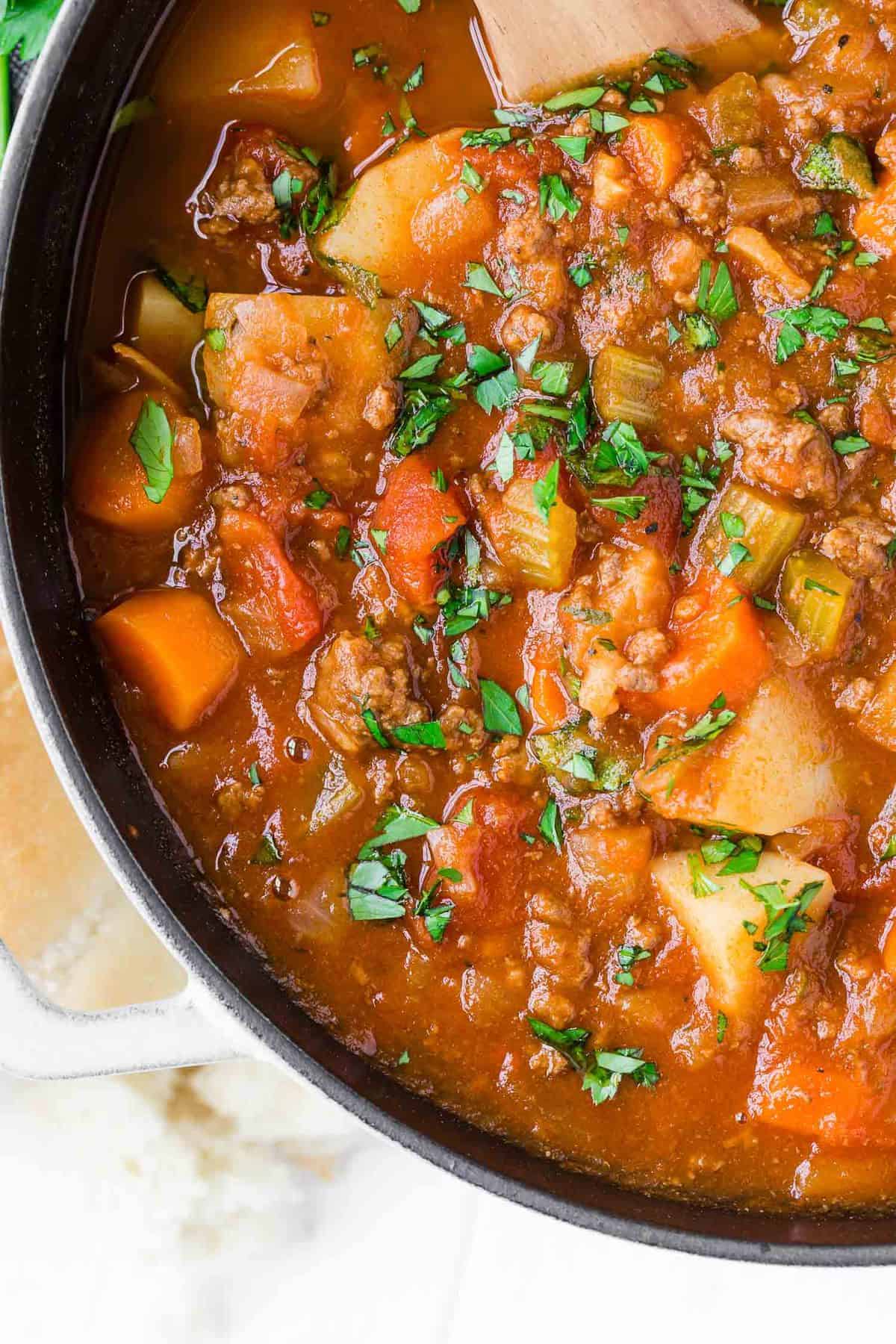 Close up of soup with ground beef, potatoes, tomatoes, carrots, and celery.