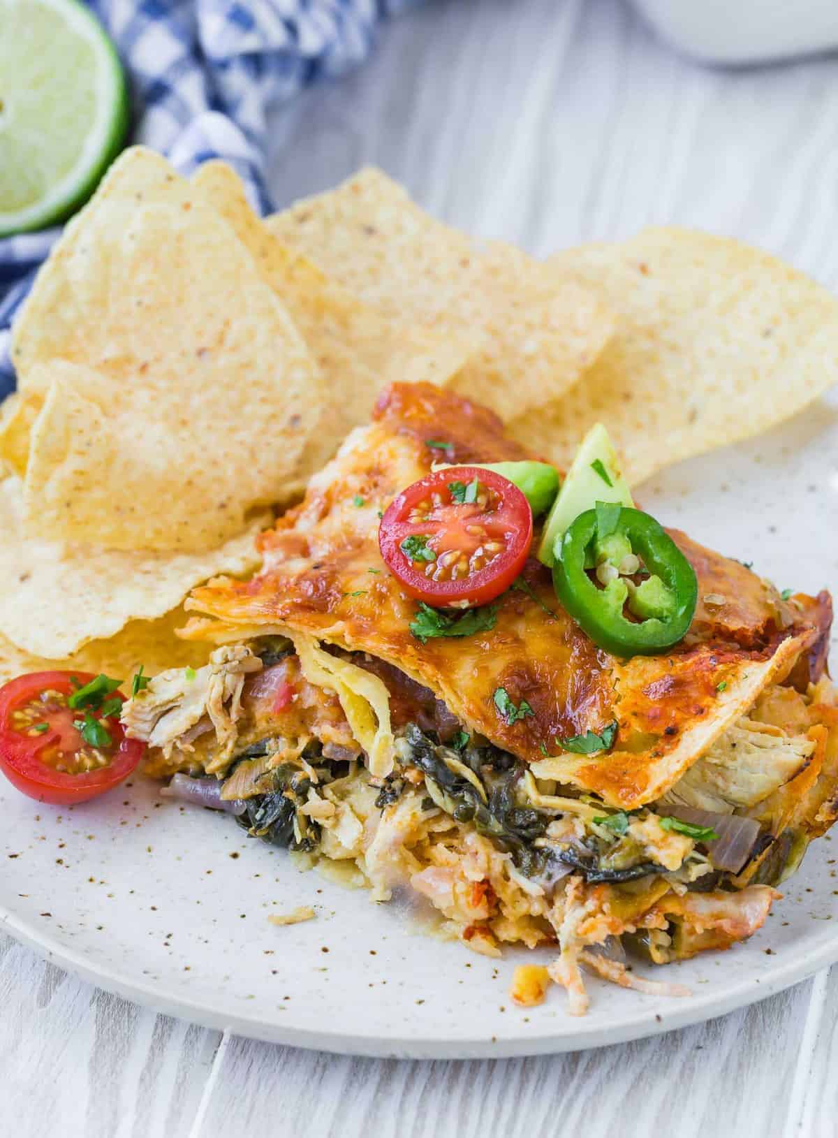 Slice of Mexican lasagna with greens on a plate with tortilla chips.