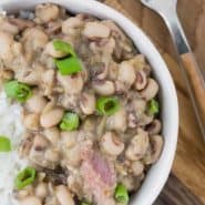 Beans, rice, and ham topped with green onions in small white bowls. Text overlay reads "hoppin' john (black eyed peas & rice), rachelcooks.com"