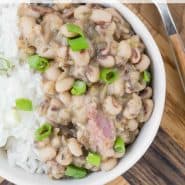 Beans, rice, and ham topped with green onions in small white bowls. Text overlay reads "hoppin' john (black eyed peas & rice), rachelcooks.com"