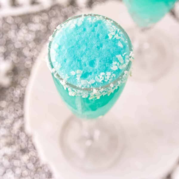 A bright blue mimosa with a coconut rim in a champagne glass.