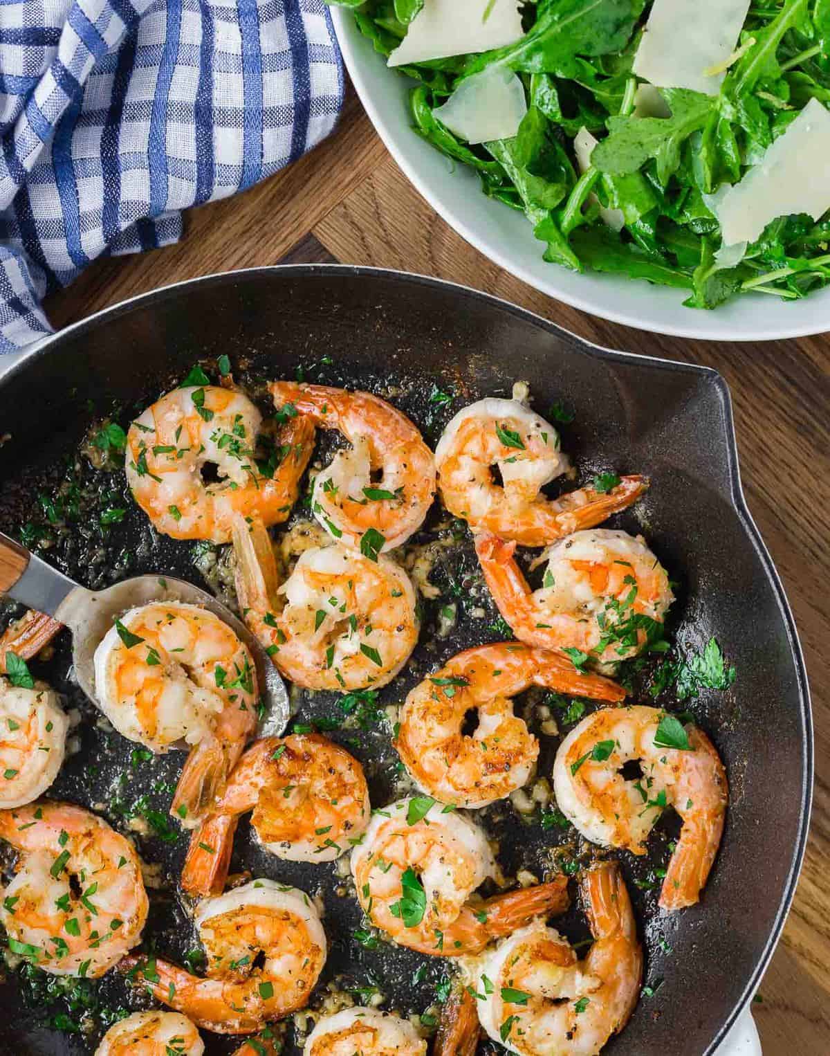 Cooked shrimp in a skillet, a green salad is partially visible.