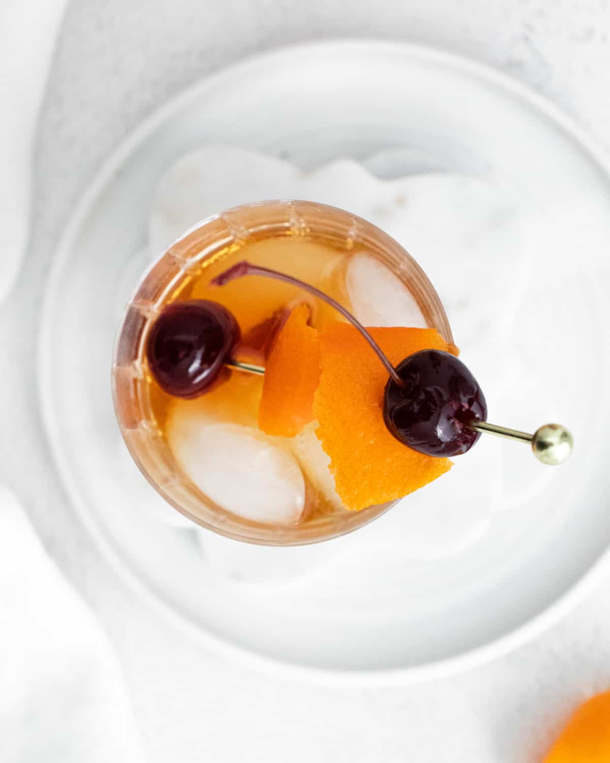Overhead view of a drink with orange peel and cherries.