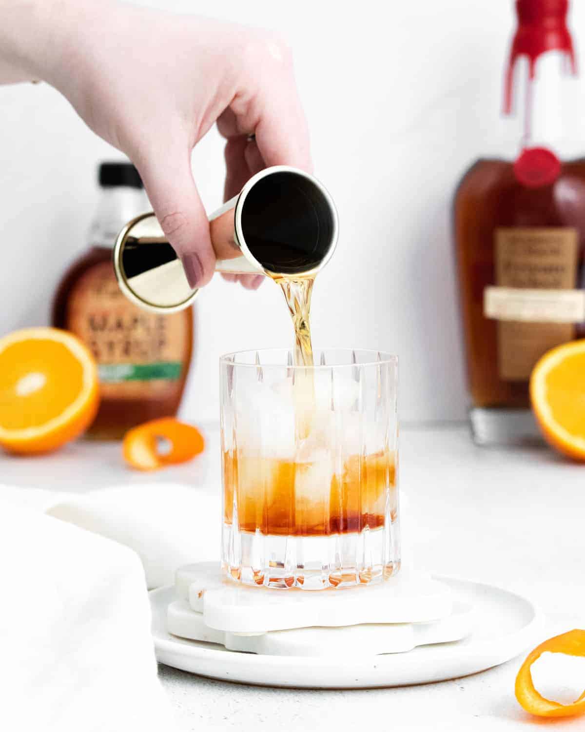 Alcohol being poured over ice in an old fashioned glass.