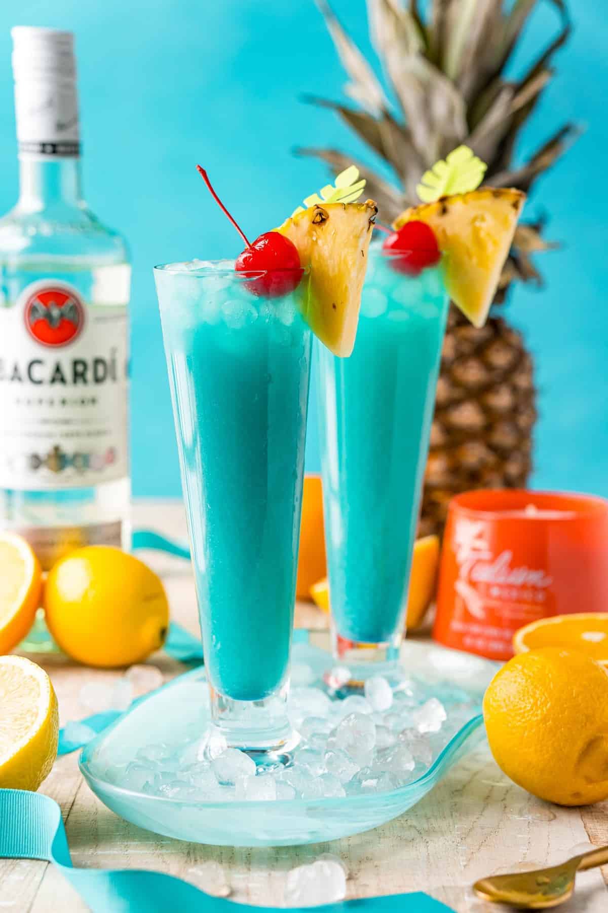Two bright blue cocktails garnished with a pineapple wedge and a cherry.