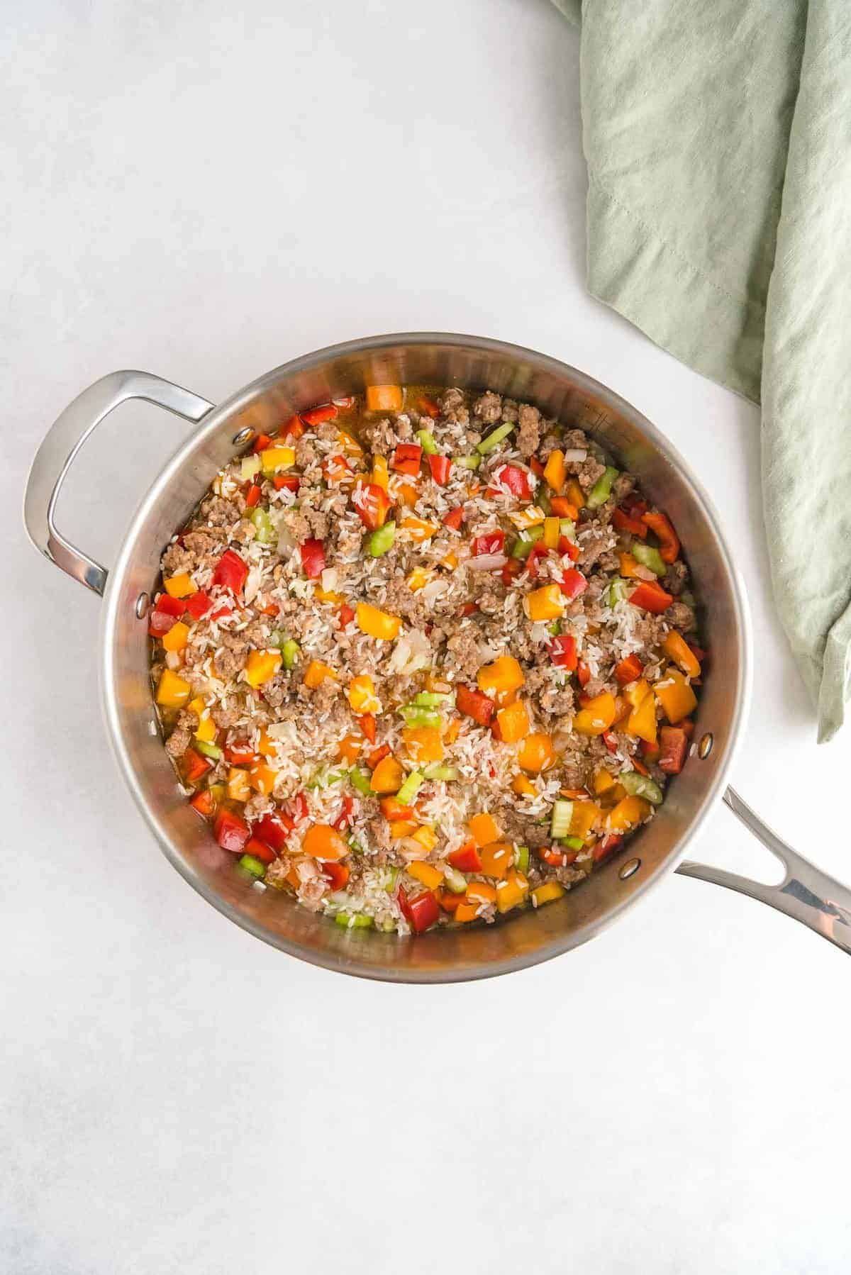 Overhead view of a saute pan full of colorful peppers, sausage, and rice.