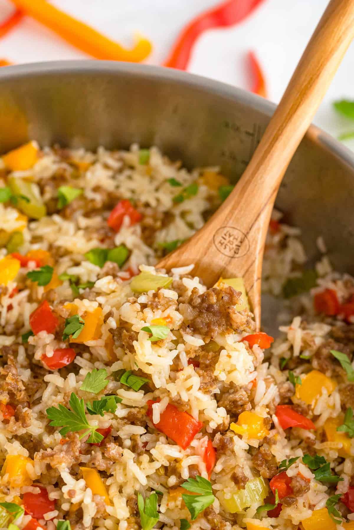 Close up of rice, sausage, and bell peppers in a skillet with a wooden spoon.