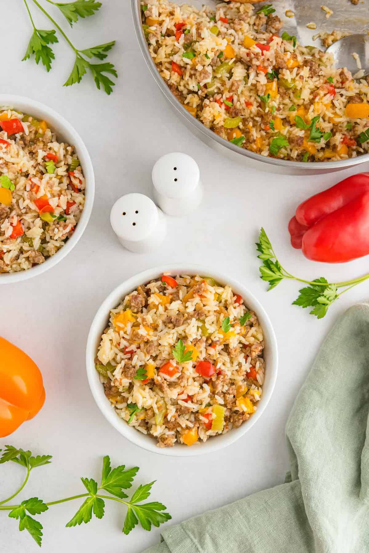 Overhead view of sausage and rice dish in small glass bowls and a pan.