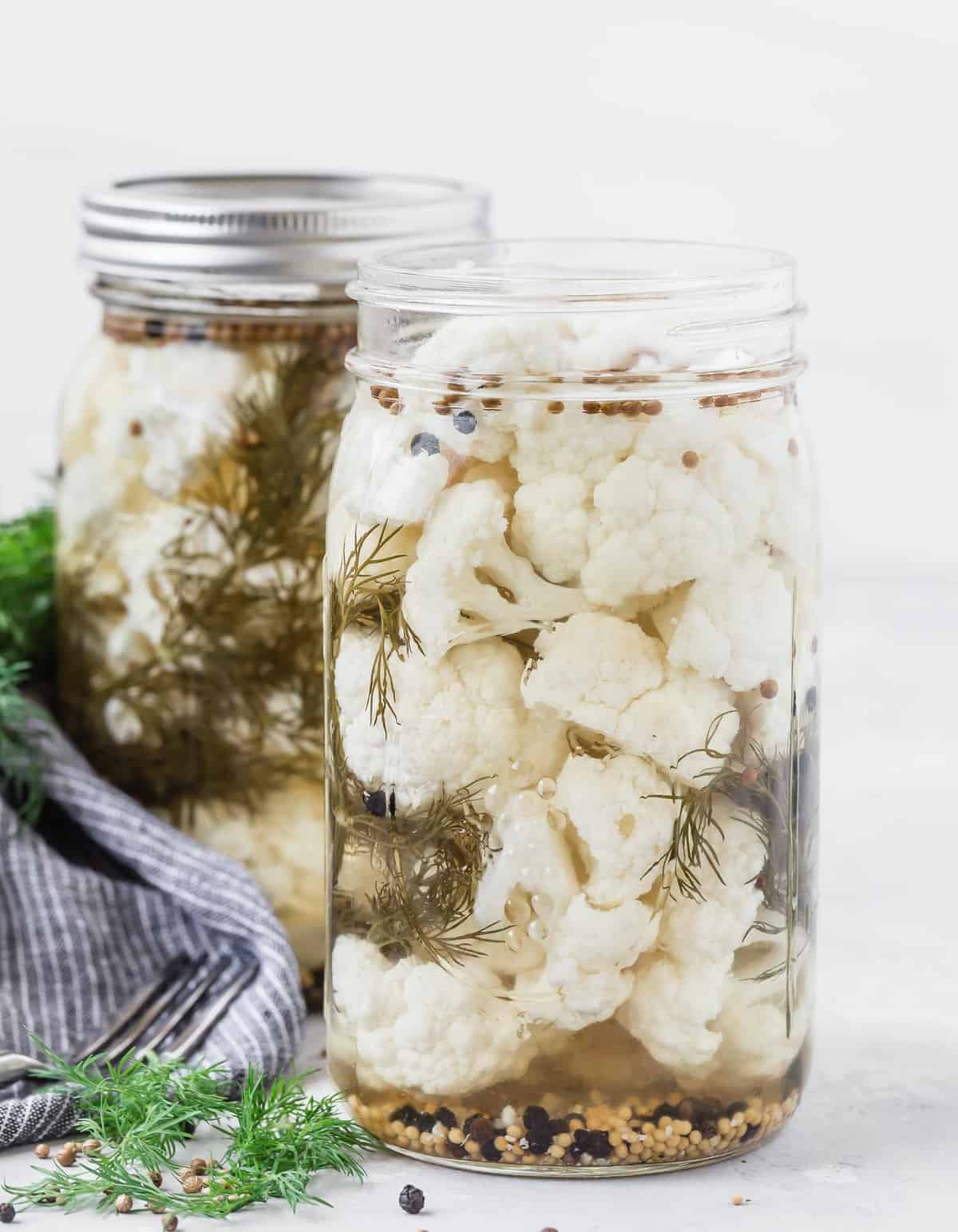 Two jars of cauliflower in pickling liquid.
