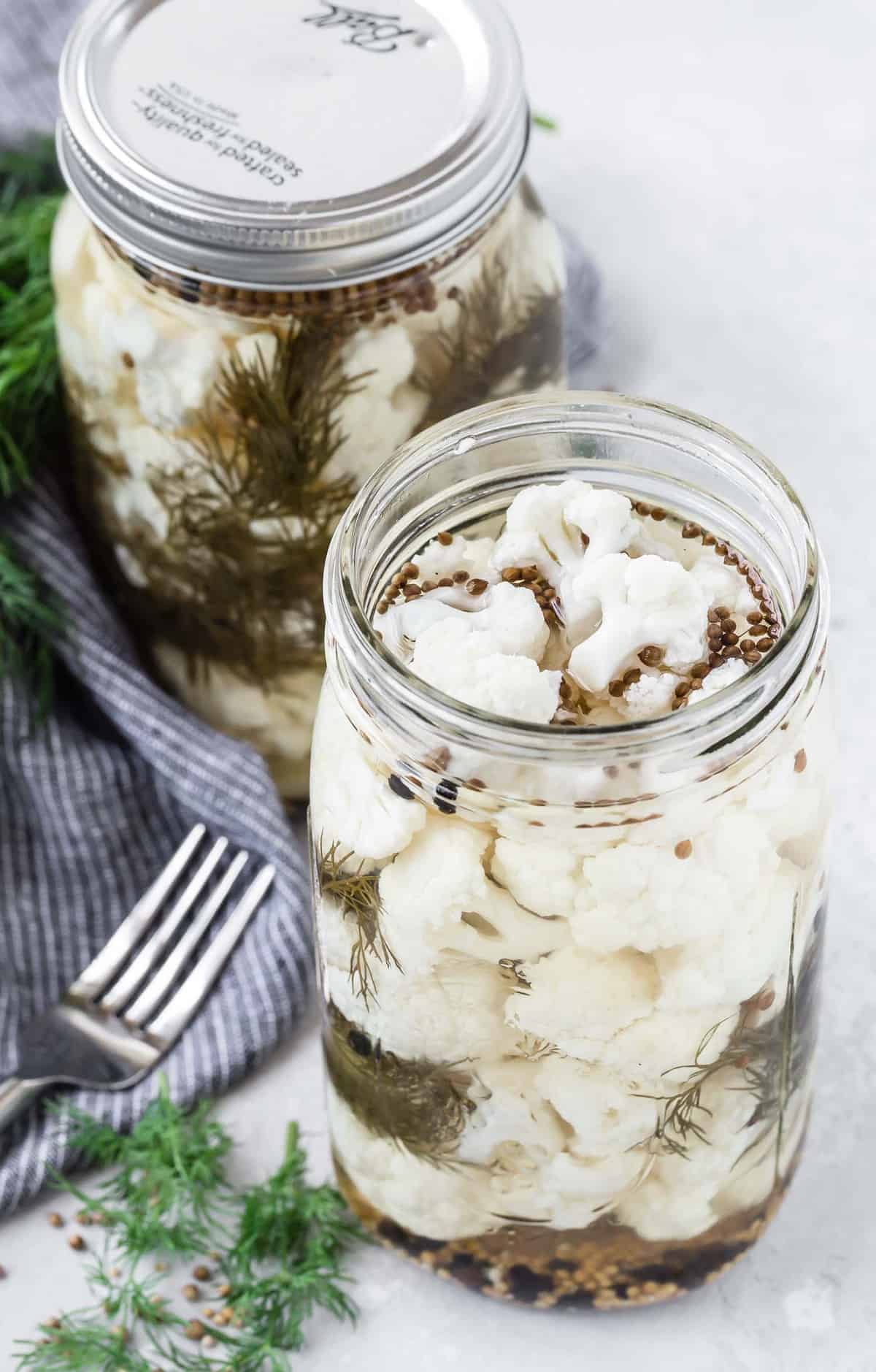 Two jars of pickled cauliflower, a fork is also pictured.