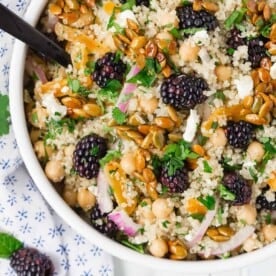 Colorful quinoa chickpea salad with blackberries, candied pepitas, onions, feta, and fresh herbs.