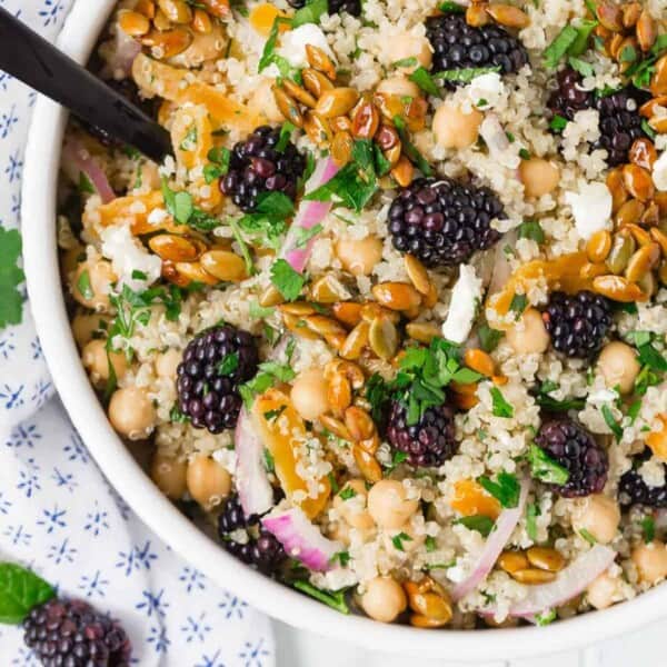 Colorful quinoa chickpea salad with blackberries, candied pepitas, onions, feta, and fresh herbs.